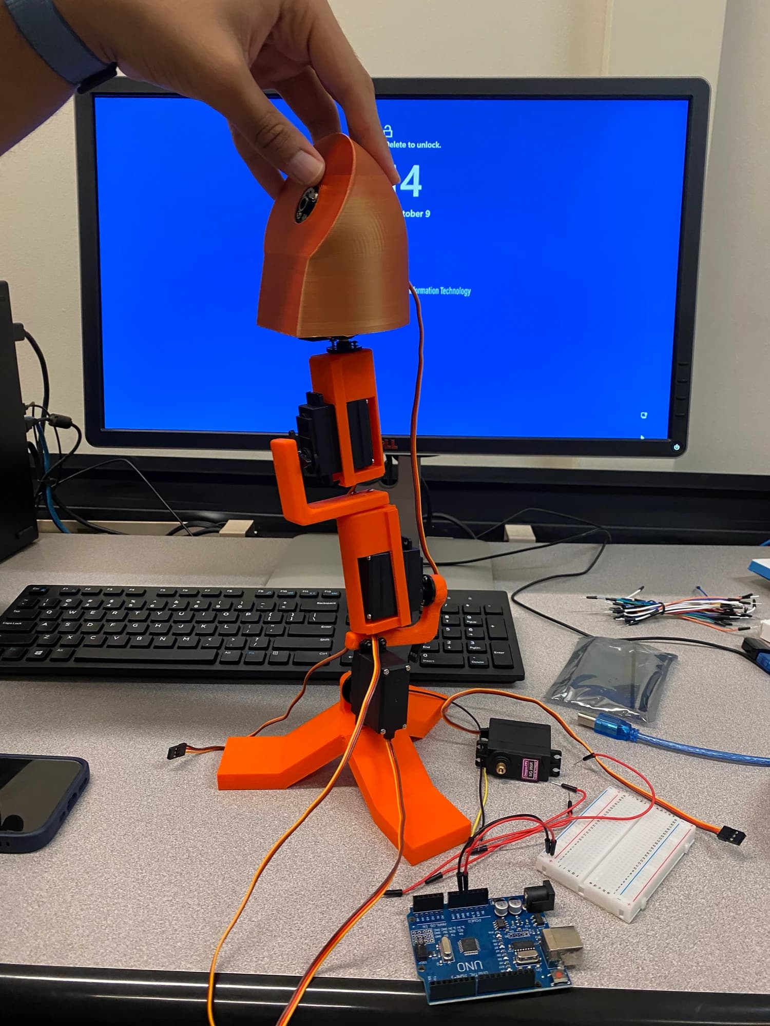 An orange robotic hand prototype at an HRC workstation