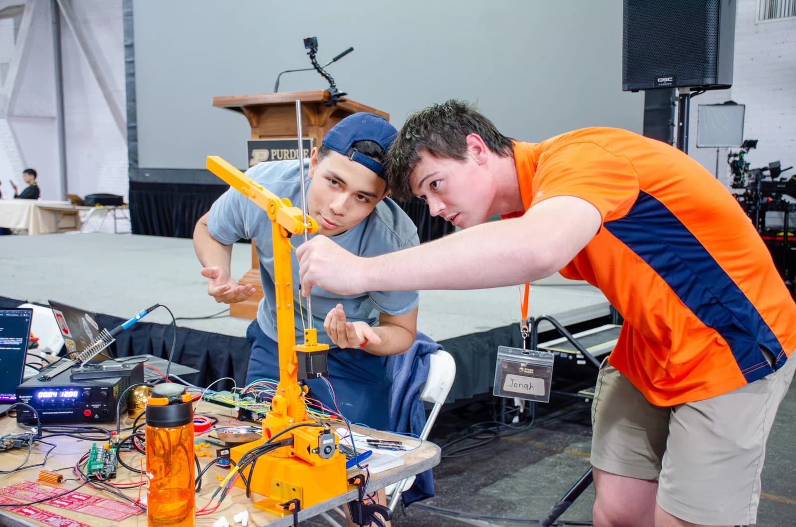 Two participants adjust an orange robotic arm at StarkHacks